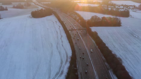 Drone-footage-of-motorway-surrounded-by-snow-in-fields-with-cars-driving-along-the-M25-in-the-morning-for-sunrise