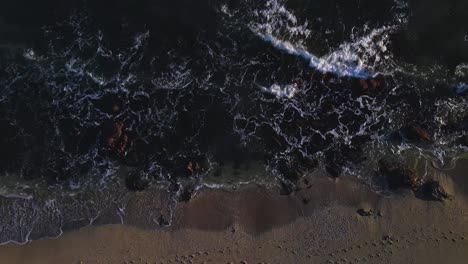Aerial-view-of-waves-at-the-beach,-moving-closer-and-tilting-up-into-the-horizon
