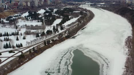 Aerial-birds-eye-view-fly-over-Groat-Rd-NW-Bridge-snow-covered-icy-North-Saskatchewan-River-on-a-winter-gloomy-afternoon-surrounded-by-quiet-golf-courses-and-the-Victoria-park-on-the-left-Alberta-4-7