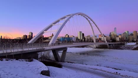 Atemberaubender-Winter-Lila-Rosa-Herrlicher-Sonnenuntergang-Edmonton-Innenstadt-Weiß-Futuristisch-Walter-Dale-Brücke-In-Einer-Postmodernen-Stadt-Radfahrerpaar-Radeln-An-Eisigen-Flussrändern,-Die-über-Dem-North-Saskatchewan-River-Zugefroren-Sind-3-3