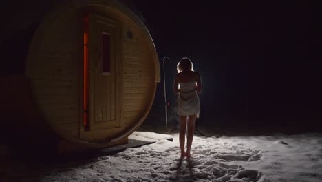 Young-slim-woman-wearing-a-towel-standing-in-the-snow-outside-a-sauna-house