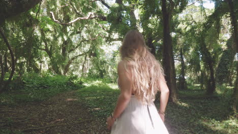 Blonde-girl-walks-in-tropical-forest,-turns-around-and-looks-into-camera