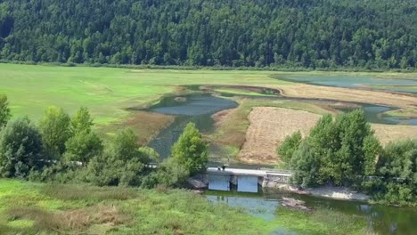 Beautiful-aerial-view-of-the-canal,-bridge,-road,-and-farm-fields-in-the-Lake-Cerknica,-river-Rak