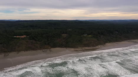 Oregon-Coast-Near-Bandon---Waves-Splashing-into-the-White-Sand-Beach-With-Green-Trees-During-Sunset---Aerial-Shot