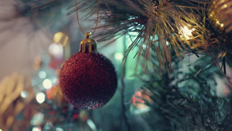 Red-Glittery-Bauble-Dangling-On-Christmas-Tree-With-Glowing-Bokeh-Lights---Closeup-Shot