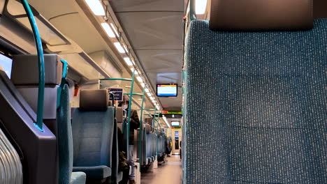 Slow-pan-right-on-railway-train-interior-showing-many-empty-seats-and-blurred-people-wearing-masks-on-background