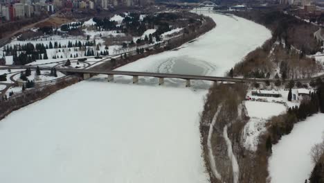 Aerial-birds-eye-view-floy-over-the-snow-coverred-icy-North-Saskatchewan-River-on-a-winter-gloomy-afternoon-surrounded-by-quiet-golf-courses-and-parks-on-each-side-seperating-the-downtown-Edmonton-2-7