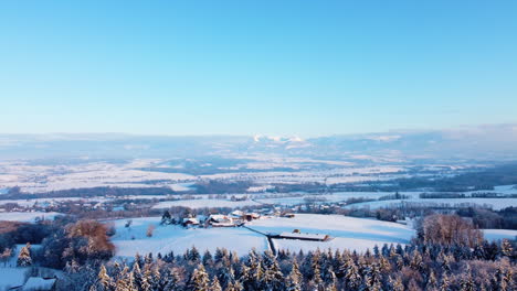Luftaufnahme-Von-Kleinen-Städten-In-Der-Nähe-Des-Schneebedeckten-Kalten-Waldes-Von-Jorat-Woods-Während-Des-Wintersonnenuntergangs,-Kanton-Waadt,-Schweiz