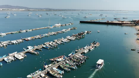 Aerial-orbiting-shot-showing-port-of-Olhao-and-fishing-boat-leaving-harbor-for-fishing-during-bright-sunny-day-in-Portugal