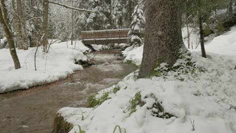 Wooden-bridge-over-a-bubbling-brook-with-snow-in-winter