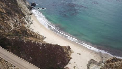 Aerial-backward-reveal-from-Big-Sur-seaside-cliff-to-Bixby-Bridge-and-car-traffic