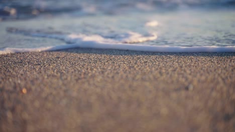 Focus-on-sand-grains-at-the-beach-with-slow-motion-waves-on-the-background