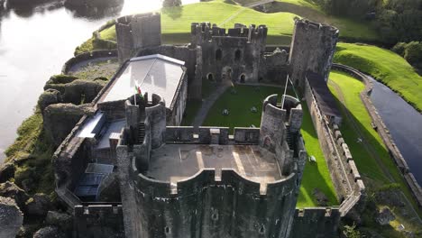 Welsh-flag-waving-on-gatehouse-of-Caerphilly-Castle,-United-Kingdom,-aerial-view