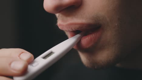 Sick-Caucasian-Man-Puts-Medical-Thermometer-In-His-Mouth-To-Check-Body-Temperature