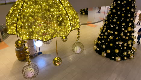 Big-Christmas-Tree-decorated-with-golden-balls-in-a-shopping-mall,-people-walking-on-background-wearing-masks