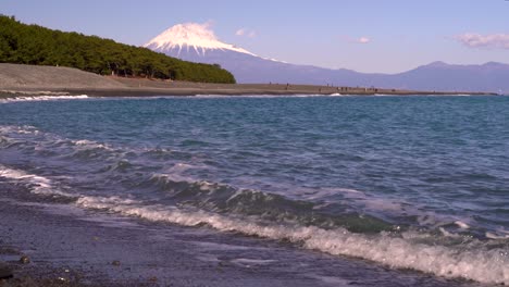 Low-angle-view-of-breaking-waves-on-beach-with-backdrop-of-Mount-Fuji-on-clear-day