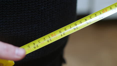 A-carpenter-man-takes-a-yellow-tape-measure-out-of-his-pocket-and-measures-in-feet-inches-and-centimeters