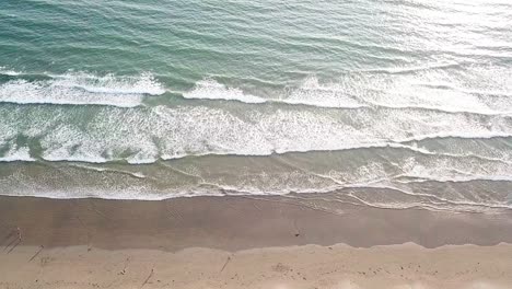 Seitlicher-Luftblick-über-Menschen-Und-Wellen,-Die-Am-Sandstrand-Brechen
