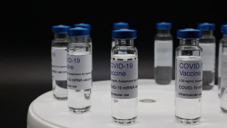 Glasfläschchen-Mit-Covid-19-Impfstoff-Auf-Rotierendem-Display-Isoliert-Auf-Schwarzem-Hintergrund
