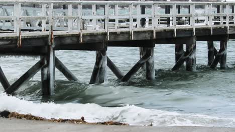 Waves-from-a-winter-storm-crash-under-a-dock-leaving-icicles-and-foam-behind