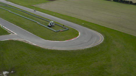 Race-car-on-a-circuit-taking-a-corner-surrounded-by-green-fields