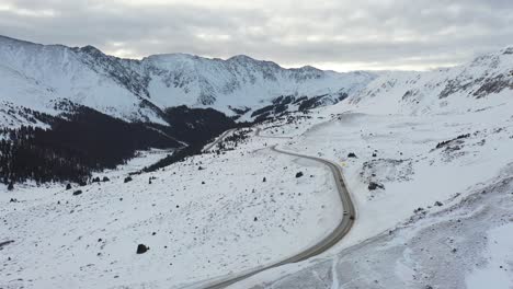 Aerial-View-of-Cars-on-Rural-Countryside-Road-in-Snowy-Winter-Landscape-of-Rocky-Mountains,-Tilt-Up-Drone-Shot