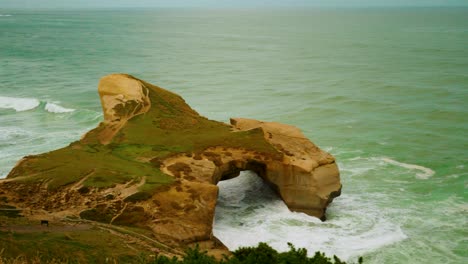 Walking-handheld-shot-of-a-sea-arch-rock-formation-along-the-coast-in-New-Zealand
