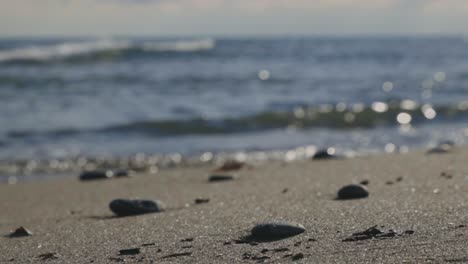 Stones-On-Sandy-Shoreline-With-Crashing-Sea-Waves-During-Sunset