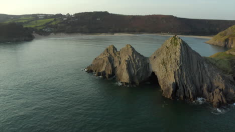 Smooth-drone-aerial-shot-of-three-cliffs-bay-with-couple-on-the-cliff-in-the-Gower,-Wales,-surrounded-by-the-sea