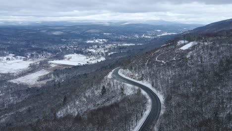 Aerial-drone-footage-of-a-scenic-highway-in-snowy-mountains-with-a-vast,-snowy-mountain-below-and-snow-capped-mountains-in-the-distance