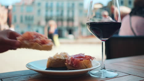Close-up-shot-of-person-eating-italian-Focaccia-Bread-with-raw-ham-and-red-wine-during-sunny-day-in-Venice,Italy