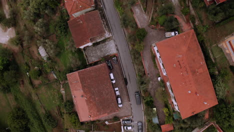 Drohne,-Die-Einem-Schwarzen-Auto-Aus-Der-Vogelperspektive-Folgt-Und-Durch-Eine-Stadt-Mit-Orangefarbenen-Dächern-Fährt,-Umgeben-Von-Natur,-Florenz,-Italien