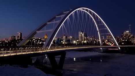 4k-Bokeh-blur-time-lapse-LOOP-sunset-winter-night-of-a-reflection-of-a-white-modern-Walter-Dale-bow-tie-bridge-with-an-icy-North-Saskatchewan-River-with-skyline-high-rise-buildings-hotels-condos-4-4