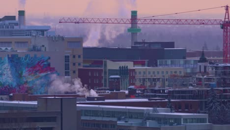 4k-Winter-twilight-University-of-Alberta-buildings-rooftops-covered-with-snow-steam-louds-puffing-with-faded-blurred-background-forest-trees-and-some-residential-housing-and-red-construction-crane