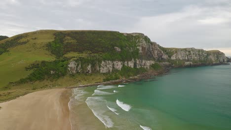 Aerial-shot-of-a-cliff-along-the-coast-in-New-Zealand-with-a-beach-in-the-foreground