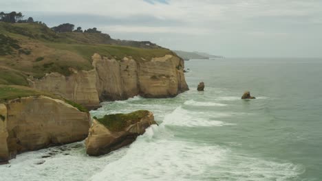 Aerial-panning-left-to-right-shot-of-islet-cliff-rock-formations-along-the-coast-in-New-Zealand