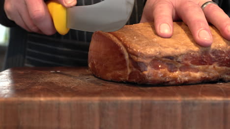 Person-slicing-whole-piece-of-back-bacon-into-thick-delicious-slices,-slider-shot