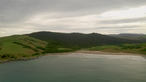 Aerial-shot-of-a-mountain-range-along-the-coastline-in-New-Zealand-with-a-sunset-in-the-background