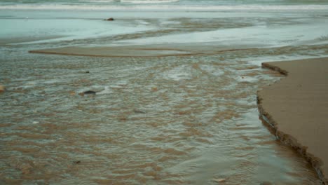Hochkippen-Eines-Baches,-Der-An-Einem-Strand-In-Neuseeland-In-Den-Ozean-Fließt-Und-Sich-Ihm-Anschließt