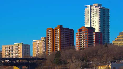 4k-Stunning-Blue-clear-sunny-afternoon-sklyline-closeup-of-post-modern-apartment-buildings-towering-over-older-condominiums-by-river-valley-of-downtown-Edmonton-next-to-historic-high-level-bridge