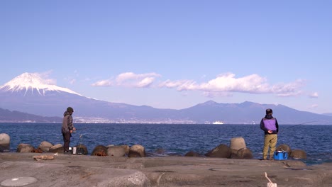 Two-fishermen-fishing-at-pier-with-backdrop-of-Mount-Fuji-in-Japan