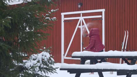 Mujer-Lanzando-Una-Bola-De-Nieve-En-Cámara-Lenta-Frente-A-Una-Casa-De-Madera-Roja-En-Noruega