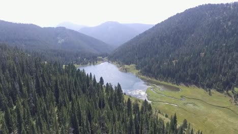 Drone-creeps-closer-to-blue-lake-surrounded-by-mountains