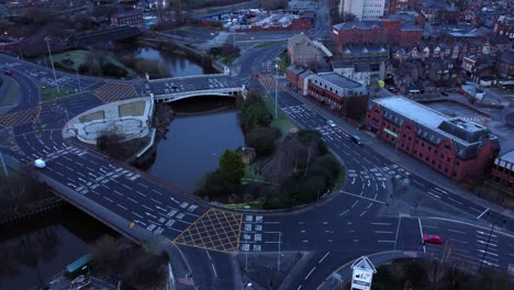Aerial-view-looking-down-city-centre-canal-roundabout-infrastructure-suburban-streets-traffic-at-daybreak-push-in-right