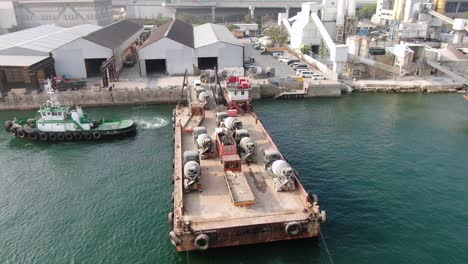 Barge-loaded-with-Concrete-mixer-trucks-pulled-to-port-by-a-Tugboat-in-Hong-Kong-bay,-Aerial-view