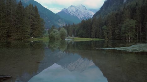 Alpine-mountain-range-reflecting-in-lake-Plansar-or-Plansarsko-jezero-in-Jezersko,-Slovenia-in-autumn,-revealing-tilt-up-shot