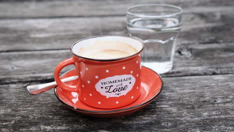 Homemade-coffee-in-red-enamel-cup-on-rustic-wooden-table-with-a-glass-of-water