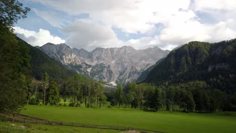 Kamnik-Savinja-Alps-from-Jezersko,-Slovenia,-clouds-above-mountains-and-meadows-with-trees-in-front