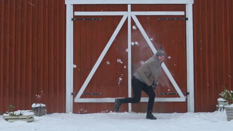 Hipster-playing-with-snowballs-in-front-of-a-red-wooden-house-in-slow-motion