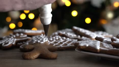 Male-chef-decorating-gingerbread-man-with-white-sugar-icing-with-Christmas-tree-in-the-background
